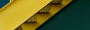 a detail image of a yellow grated stairway infront of a green building